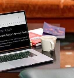 Laptop on a table displaying a blog dashboard with a cup of coffee and books in the background