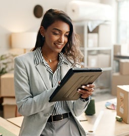 Smiling businesswoman works on a tablet surrounded by packing boxes