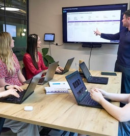 A group of professionals attending a presentation led by a confident presenter pointing at a screen displaying graphs.