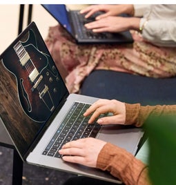 Woman uses her laptop to build a music website, with a large guitar image visible on her screen.