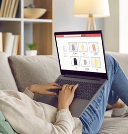 Photo of a woman lying down on a sofa browsing an online store on her lap