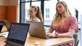 Two focused women working on laptops in a bright office environment