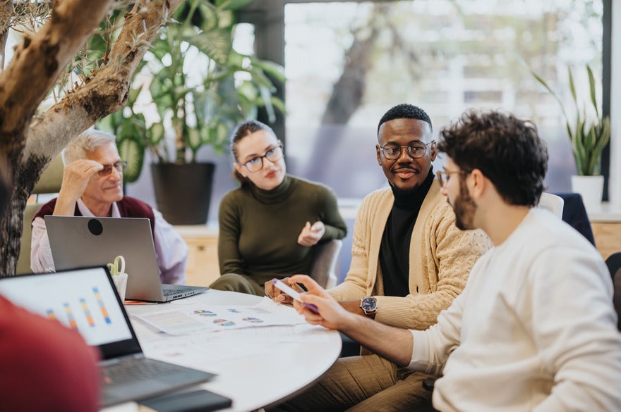 Group of office workers chatting around a table with laptops and paper in front of them