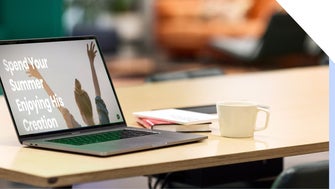 Laptop on a desk, displaying a summer Bible camp message on-screen, alongside a coffee cup and notebook on the desk.