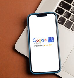 Phone showing Google Reviews logo, resting on a laptop