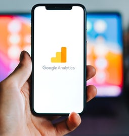 Hand holding a mobile device with the Google Analytics logo on the screen