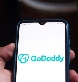 A person holding a smartphone with a GoDaddy logo on the screen.