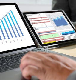 Photo of a laptop and a tablet with graph data on the screen