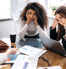 Group of people looking stressed around a work table as if trying to solve a problem