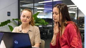 Two professional women collaborating on a project using a laptop in an office setting.