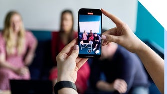 A close-up of a smartphone taking a video of friends for social media, with a blurred background.