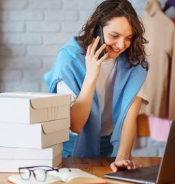 A woman on a laptop at her desk on the phone and with parcels