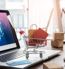 A laptop with a small on trolley with shopping bags on the keyboard.