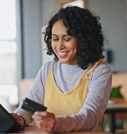 Smiling woman holds her credit card while looking at her ipad