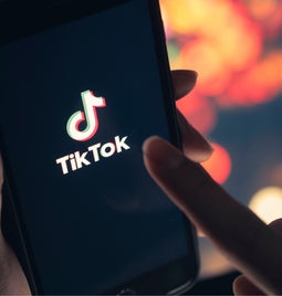 Hands holding a mobile device showing the TikTok logo on screen