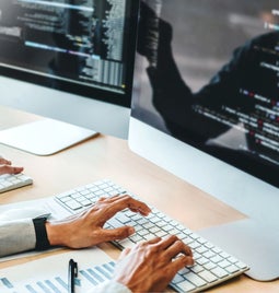 Screenshot of two hands typing on desktops with code on them