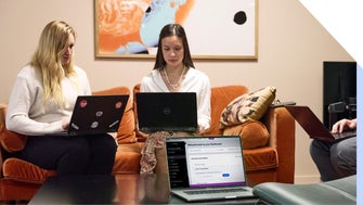 Two individuals working on laptops in a cozy co-working space, with a third laptop on the desk facing an empty chair, showing a Wix dashboard.